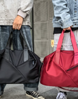Two people holding a black and a red bag respectively, standing outdoors.