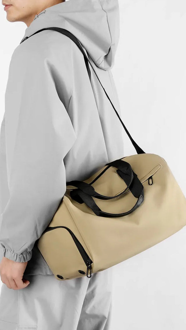 Person wearing a gray raincoat with a beige duffel bag over one shoulder on a white background