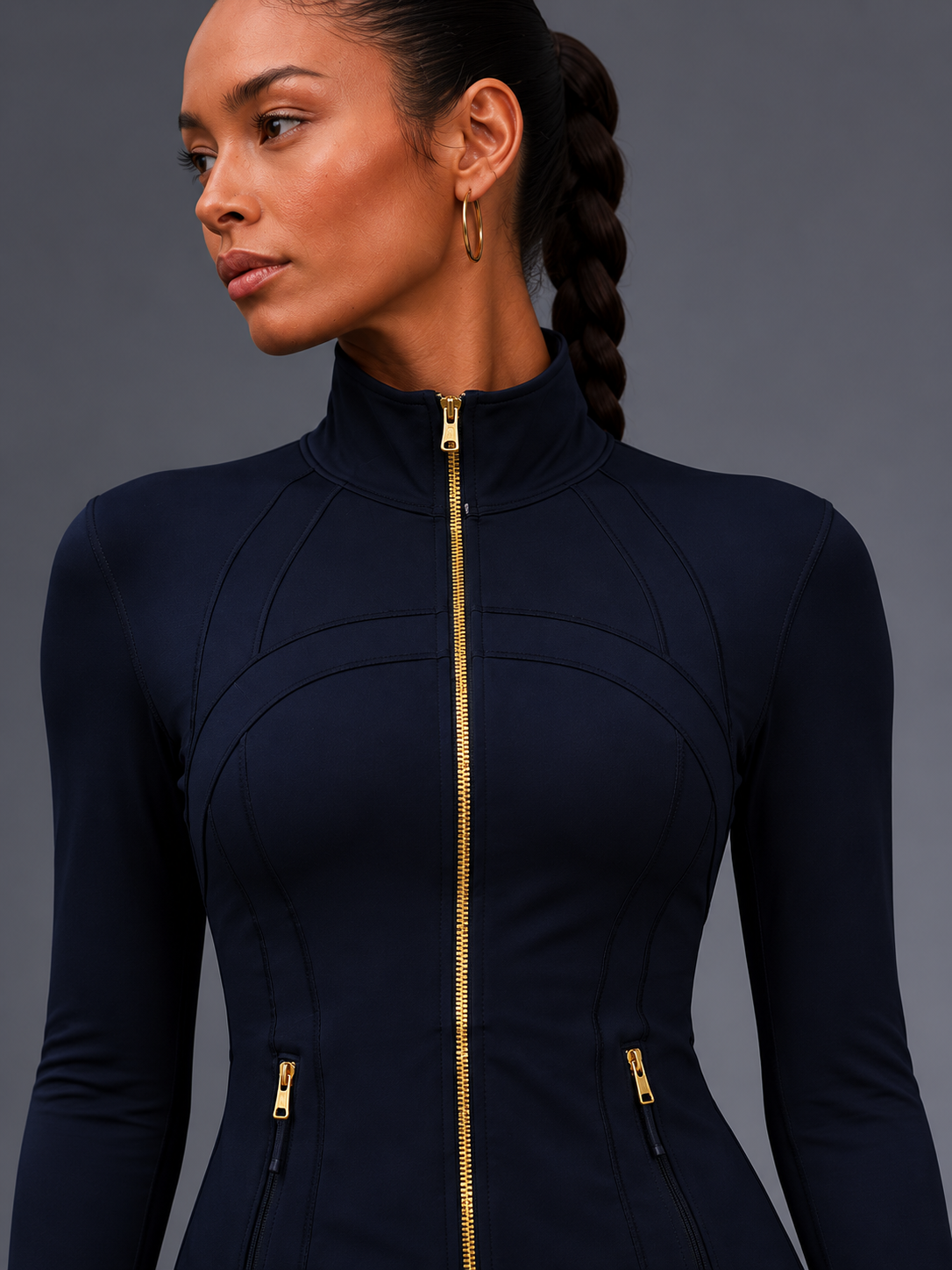 Woman wearing a navy blue outfit with gold zippers against a gray background