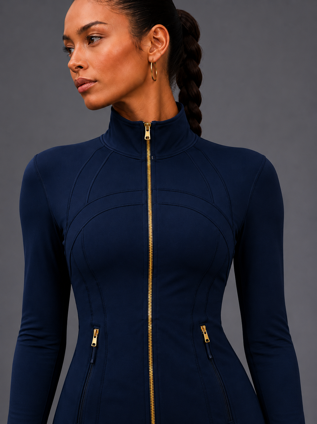 Woman wearing a navy blue long-sleeve top with gold zipper details on a gray background