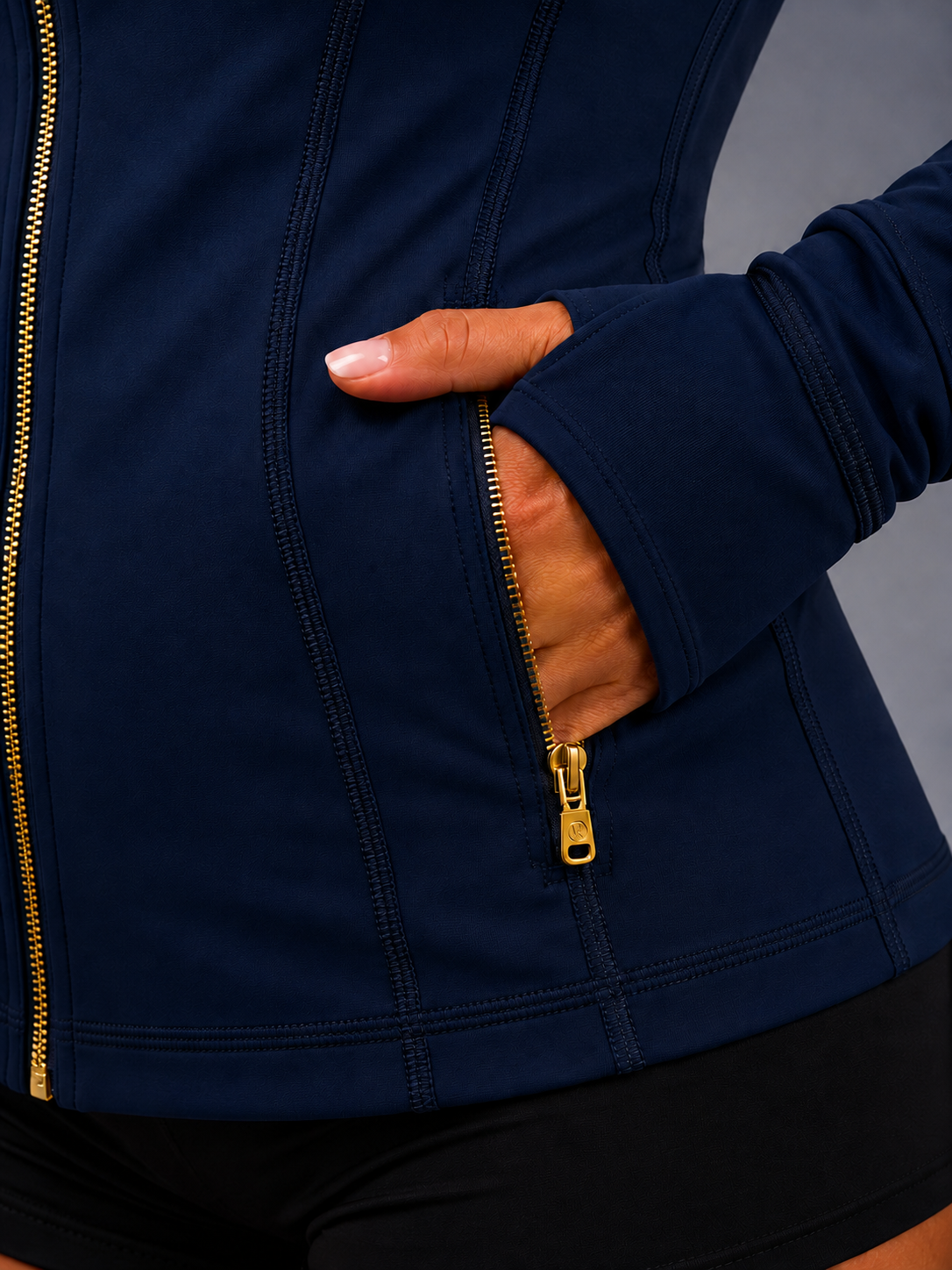 Navy blue jacket with gold zipper and hand in pocket against a gray background