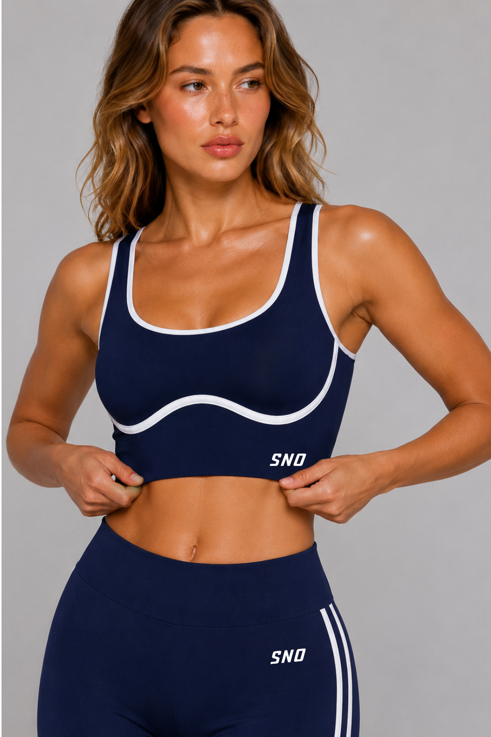 Woman wearing a navy sports bra and leggings with 'SNO' branding on a gray background