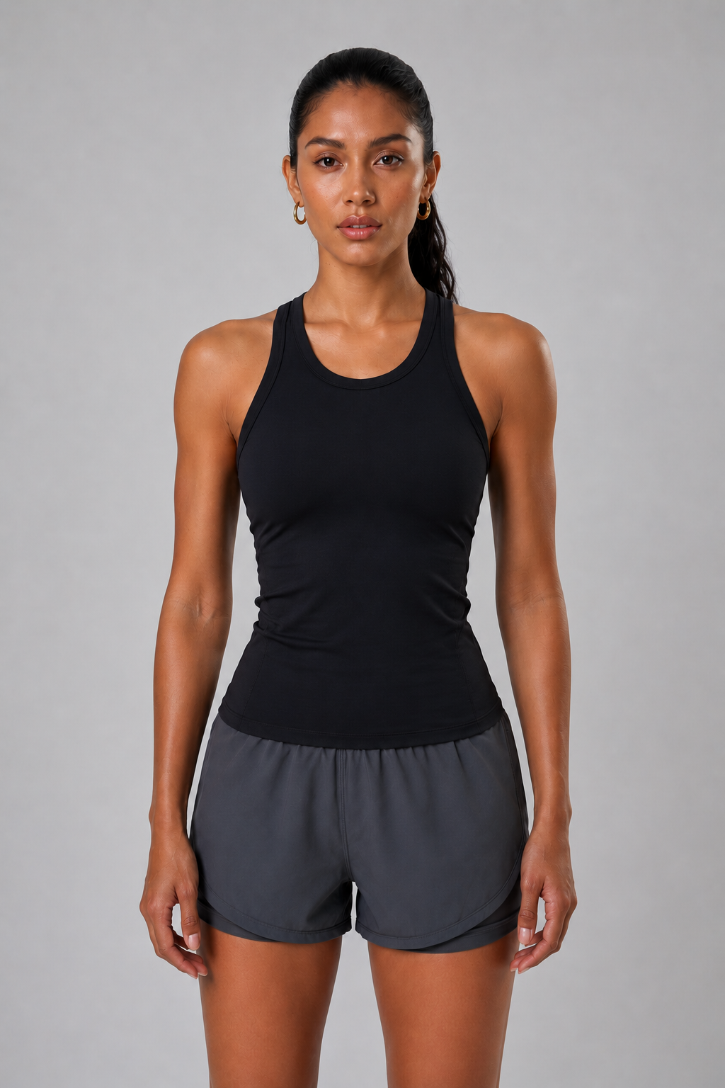 Woman wearing a black tank top and gray shorts on a gray background