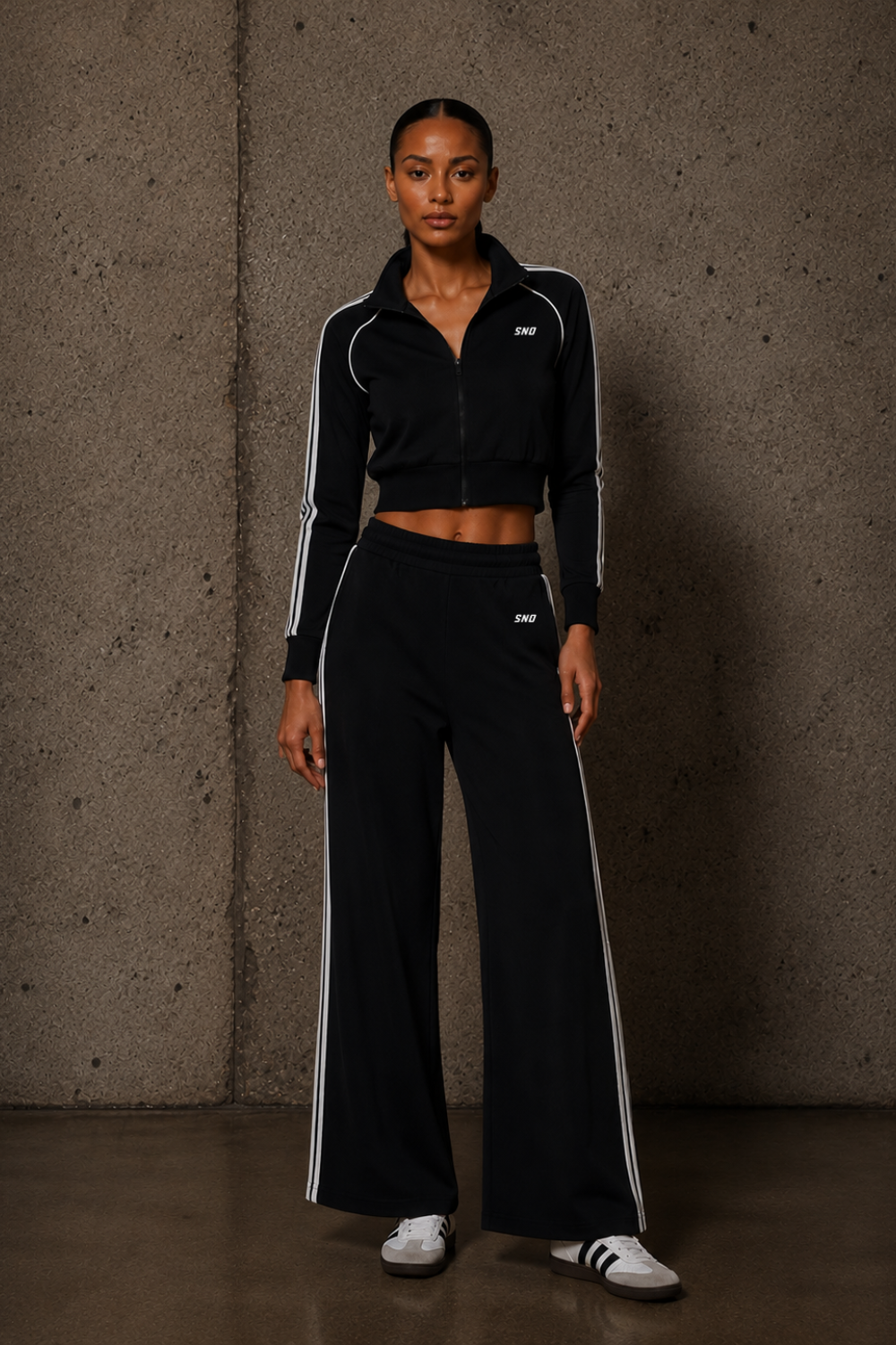 Woman wearing a black tracksuit with white stripes against a textured wall.