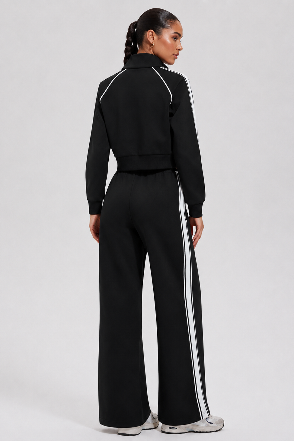 Person wearing a black tracksuit with white stripes on a light gray background