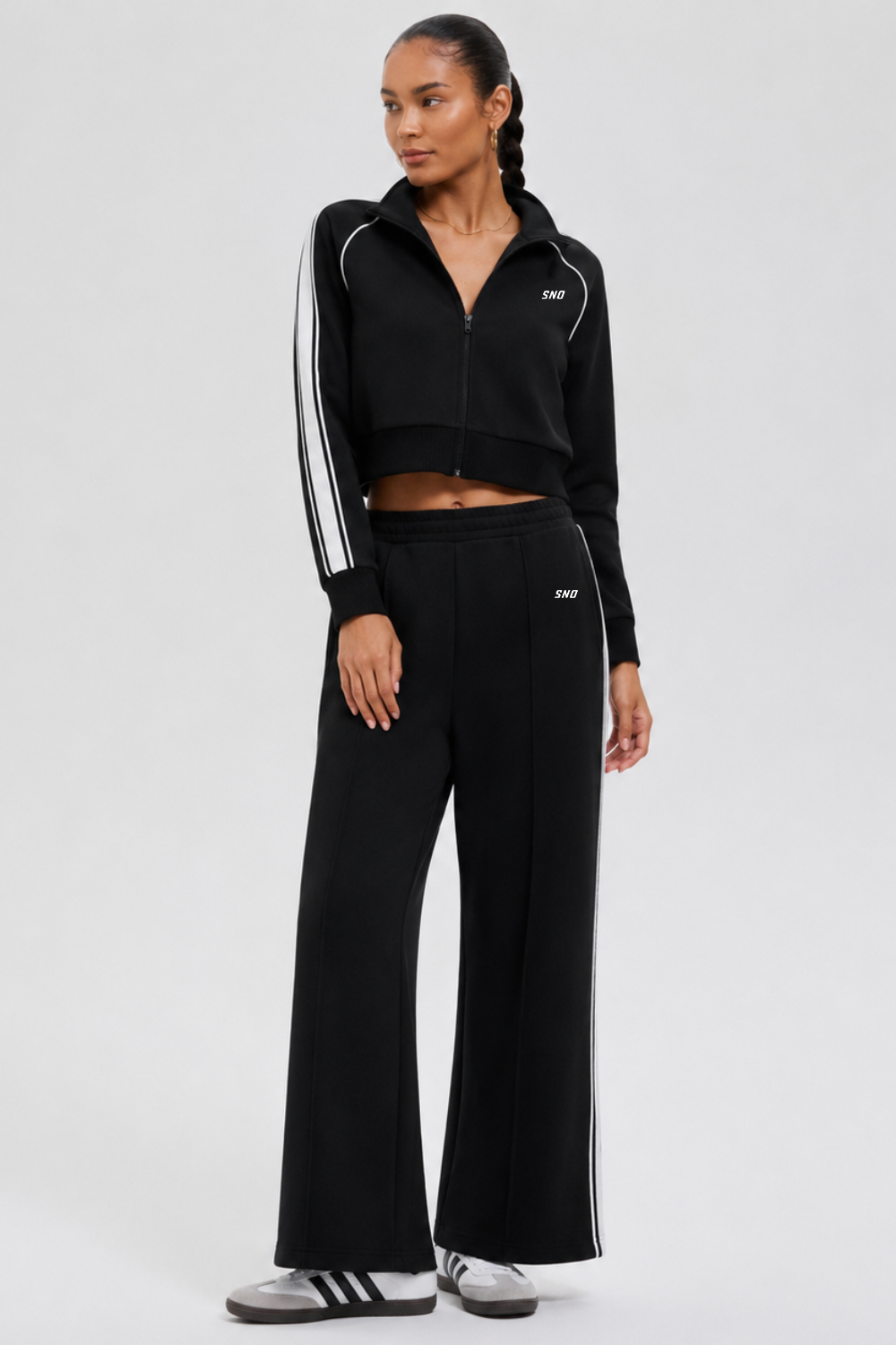Woman wearing a black tracksuit with white stripes on a light gray background