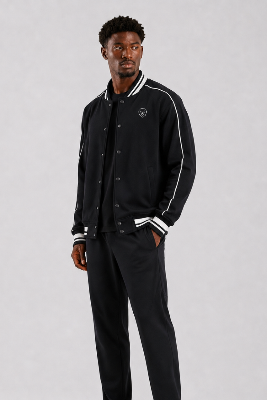 Man wearing a black varsity jacket with white accents on a gray background