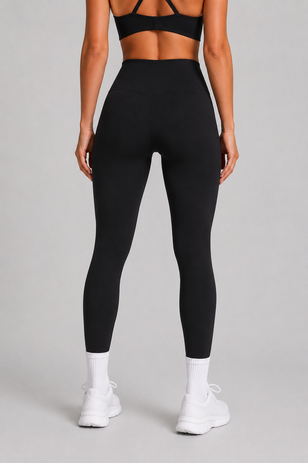 Person wearing black leggings and a black sports bra on a gray background