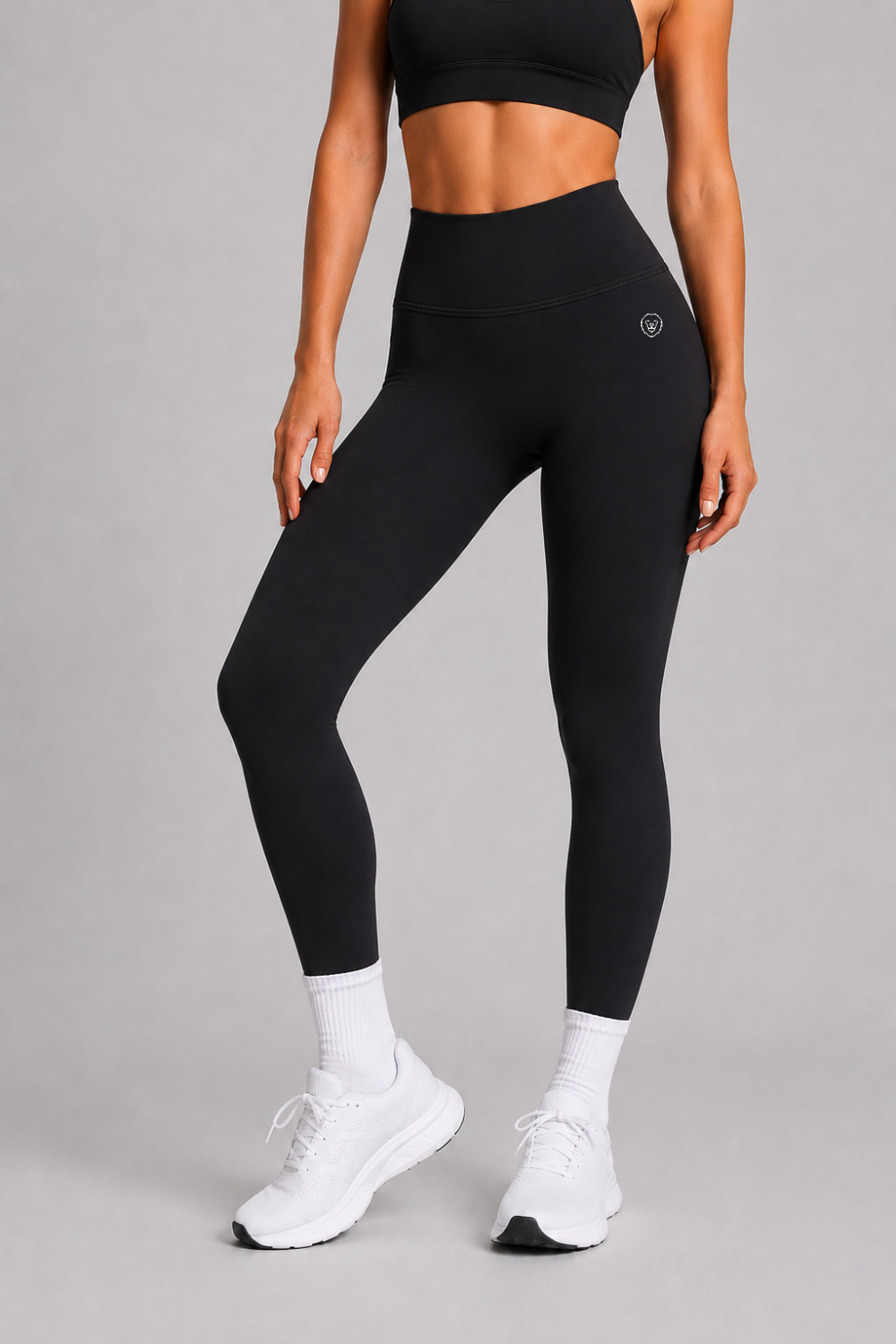 Person wearing black athletic leggings and sports bra on a gray background