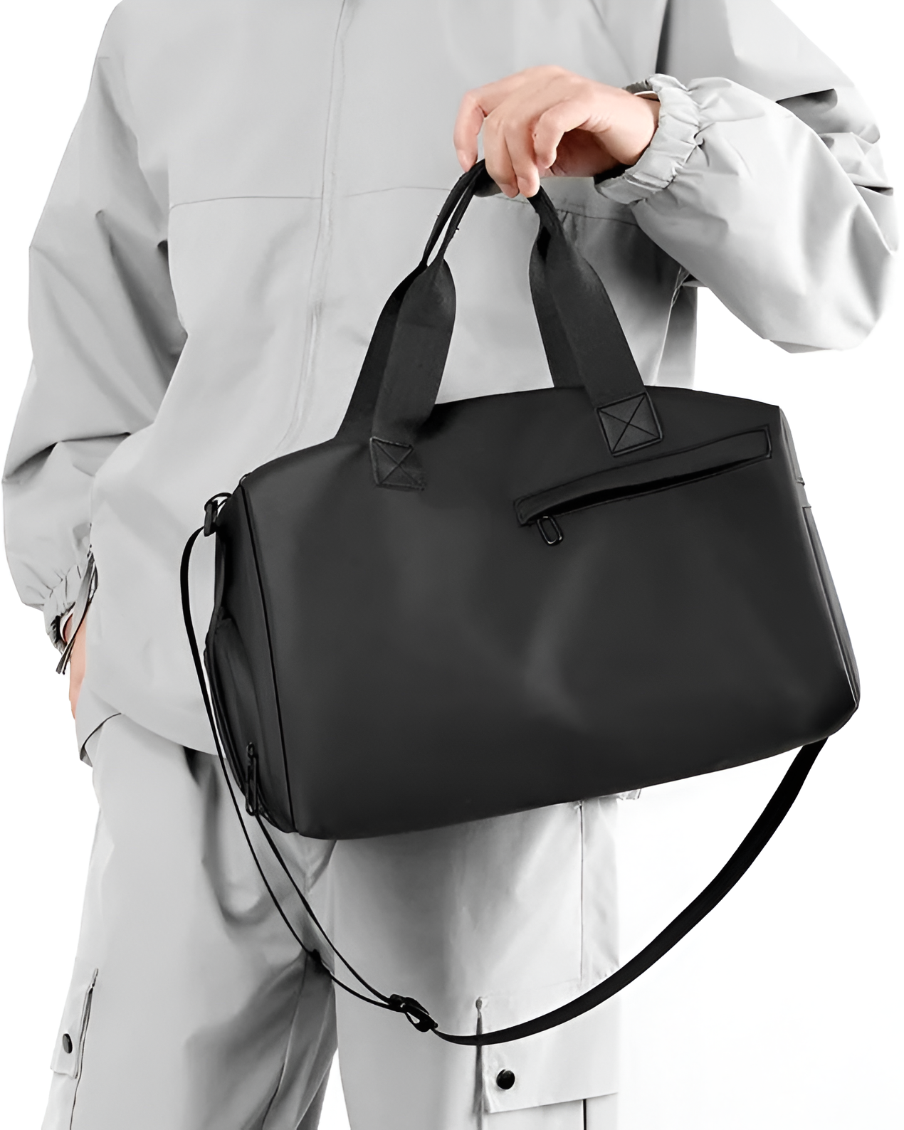 Person holding a black duffel bag against a neutral background