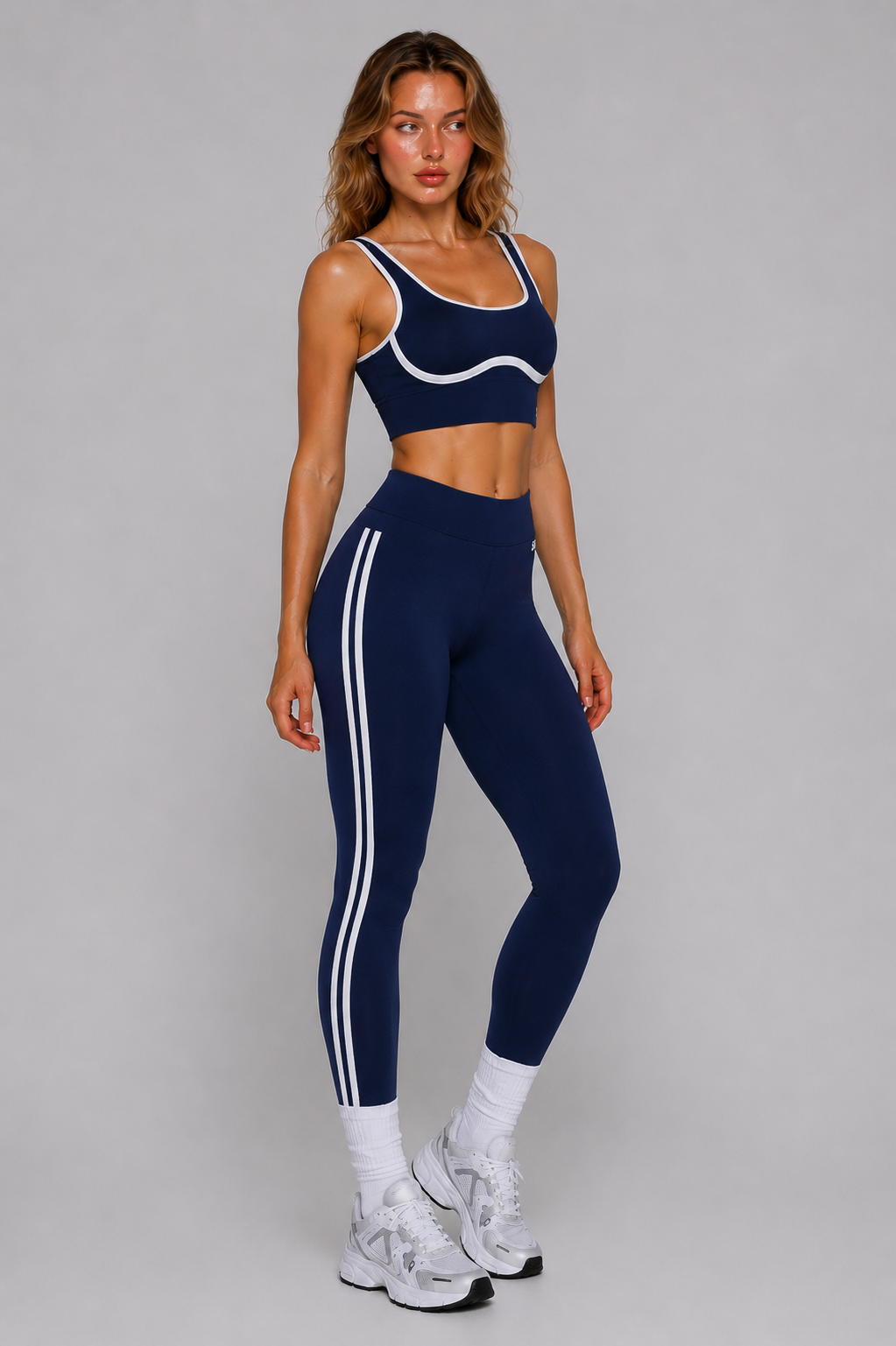 Woman wearing a navy sports bra and leggings with white stripes on a gray background
