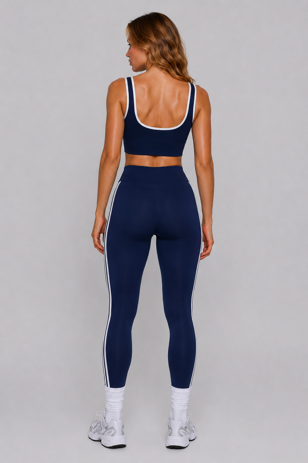 Woman wearing a navy sports bra and leggings with white accents on a gray background