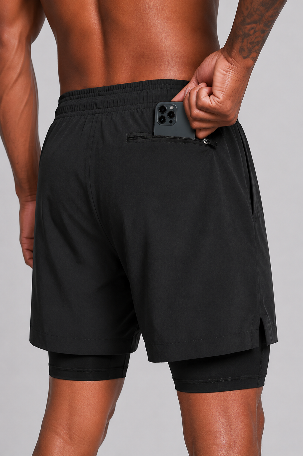 Person wearing black athletic shorts with a phone in the pocket on a gray background